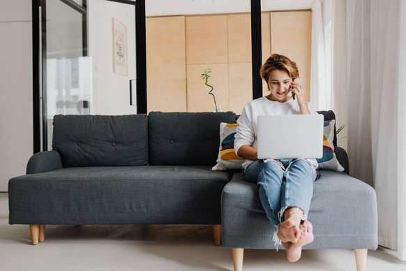 Photo d'une associée de SCI assise sur son canapé, avec son ordinateur portable. Elle veut vendre ses parts de SCI sans plus-value immobilière du particulier.