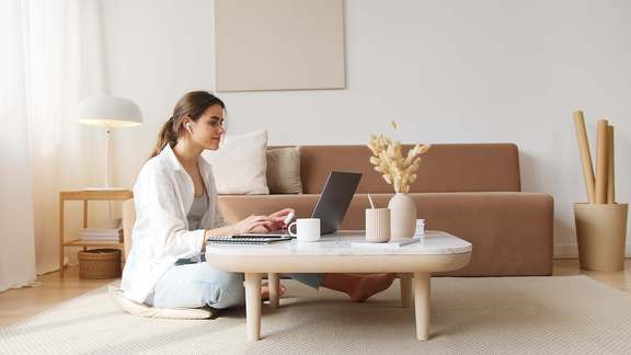 Photo d'une associée de SCI assise par terre dans son salon. Elle consulte sur son pc portable la transmission de parts de SCI.