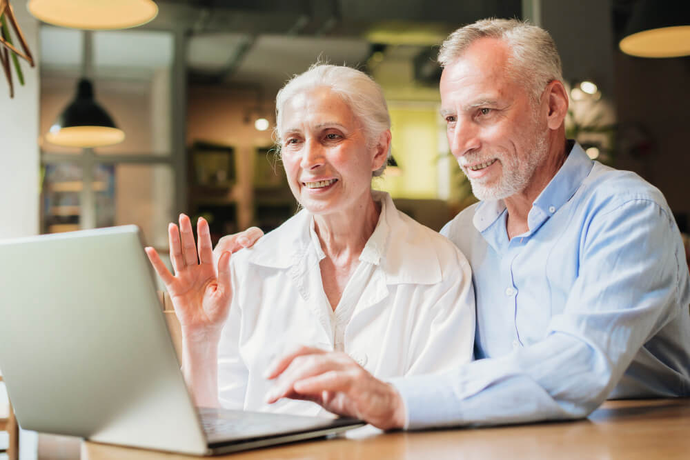 Un couple de retraités souriants devant un ordinateur pour comparer un devis mutuelle santé pour senior.