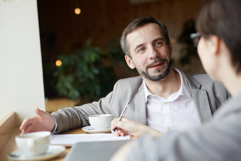 Un conseiller souriant explique les démarches pour optimiser une assurance emprunteur lors d'un rendez-vous client.