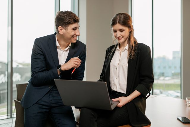 Deux courtiers d'assurances souriants consultant un ordinateur portable pour vérifier les démarches de portabilité mutuelle d'entreprise.