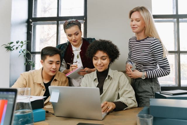 Un groupe de quatre collaborateurs réunis autour d'un ordinateur pour se renseigner sur la prévoyance d'entreprise obligatoire.