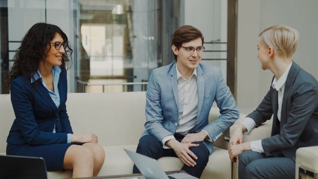 Un courtier d'assurance échangeant dans un salon professionnel avec deux dirigeantes pour définir le contrat de mutuelle santé collective de leur entreprise.