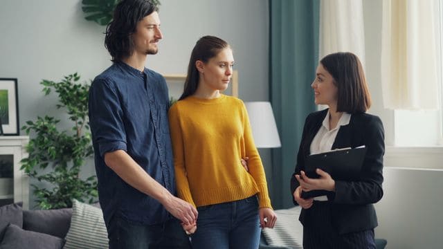 Un couple serein écoutant une courtière en assurance présenter les avantages d'une assurance emprunteur forfaitaire lors d'une simulation immobilière.